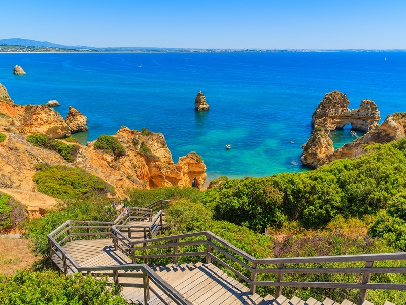 What to visit in Portugal? Wooden footbridge walkway to beautiful beach Praia do Camilo on coast of Algarve region, Portugal